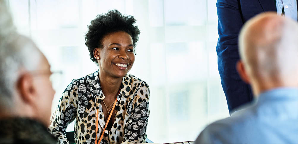 Cheerful woman in her 30s in business meeting with colleagues, smiling and listening, confidence, expertise, team player