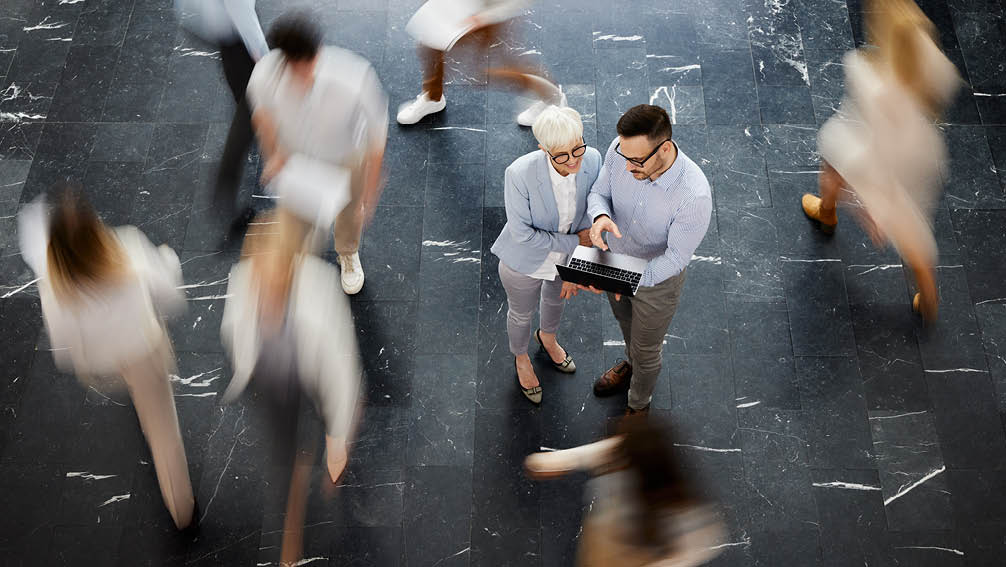 High angle view of happy business colleagues working on a computer in a hallway. Their coworkers are in blurred motion.